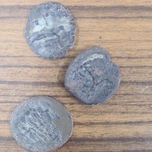 Puede incluir: Tres monedas antiguas de color plateado con superficies desgastadas. Las monedas son redondas y tienen bordes elevados. Las monedas est&aacute;n sobre una superficie de madera.