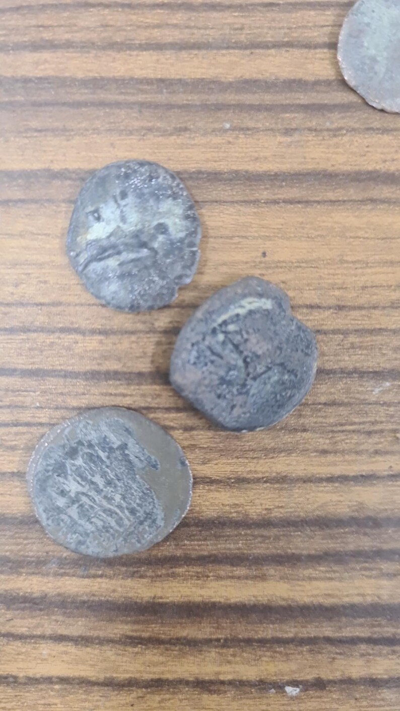 Puede incluir: Tres monedas antiguas de color plateado con superficies desgastadas. Las monedas son redondas y tienen bordes elevados. Las monedas est&aacute;n sobre una superficie de madera.