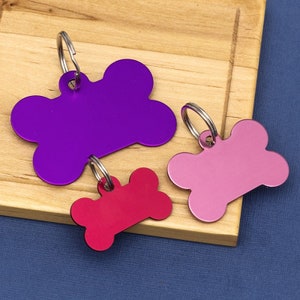 Könnte beinhalten: Drei Hundefell-förmige Haustier-ID-Tags in Lila, Rosa und Rot.
