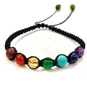 Puede incluir: Un brazalete de cordón negro con siete cuentas de piedras preciosas de colores. Las cuentas son rojas, naranjas, amarillas, verdes, azules, índigo y violetas.