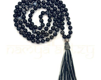 May include: Black agate mala beads with a black and white tassel. The mala is a string of beads used for meditation and prayer.