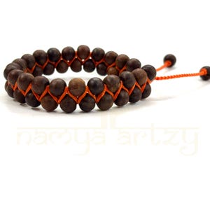 May include: A brown wooden bead bracelet with an orange cord. The bracelet has a double row of beads and a sliding knot closure.