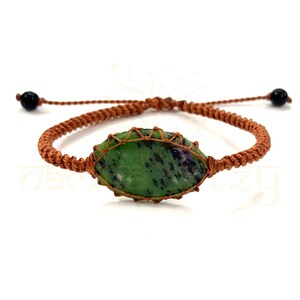 Pode incluir: Um bracelete de corda trançada marrom com uma gema verde e preta envolvida em fio de cobre.