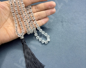May include: A white crystal beaded necklace with a black tassel. The necklace is made of round beads and has a silver clasp.