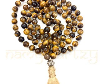 May include: A brown and gold tiger's eye mala bead necklace with a silver tassel and a silver charm. The mala is made of 108 beads and is approximately 18 inches long.