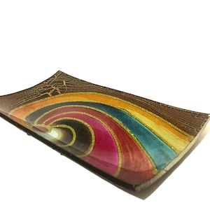 May include: Rectangular decorative glass dish with a rainbow design. The dish has a brown, cracked border and a vibrant interior with swirls of pink, orange, yellow, teal, and gold glitter accents. The dish is slightly curved.