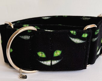 May include: Black and green dog collar with a repeating pattern of a cat's face with green eyes and a wide grin. The collar has a silver D-ring and a silver heart charm.