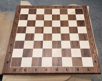 Puede incluir: Un tablero de ajedrez de madera con un patrón de tablero de ajedrez marrón claro y marrón oscuro. El tablero está etiquetado con los números del 1 al 8 en los lados y las letras de la A a la H en los extremos.