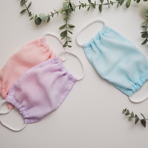 May include: Four fabric face masks in pink, light purple, and light blue. The masks are made of a soft, breathable material and have a gathered design.