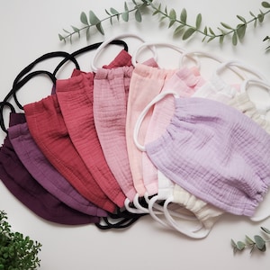 May include: A set of ten face masks in various shades of pink, purple, and red. The masks are made of a soft, breathable fabric and have elastic ear loops.