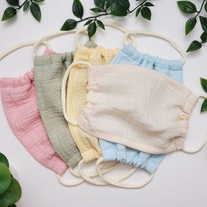 May include: Set of five face masks in various colours, including pink, green, yellow, cream, and blue. The masks are made of a soft, breathable fabric and have elastic ear loops.