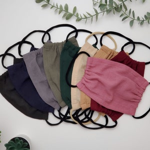 May include: A set of 10 face masks made from a soft, textured fabric. The masks are in various colours, including black, navy blue, grey, green, beige, and pink. The masks are all folded and have elastic ear loops.