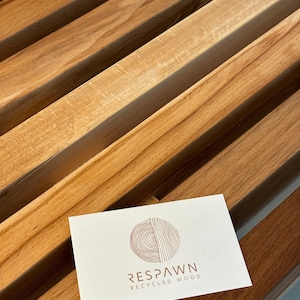 Une carte de visite blanche avec le logo de la marque Respawn Recycled Wood posée sur les lattes en bois du banc.