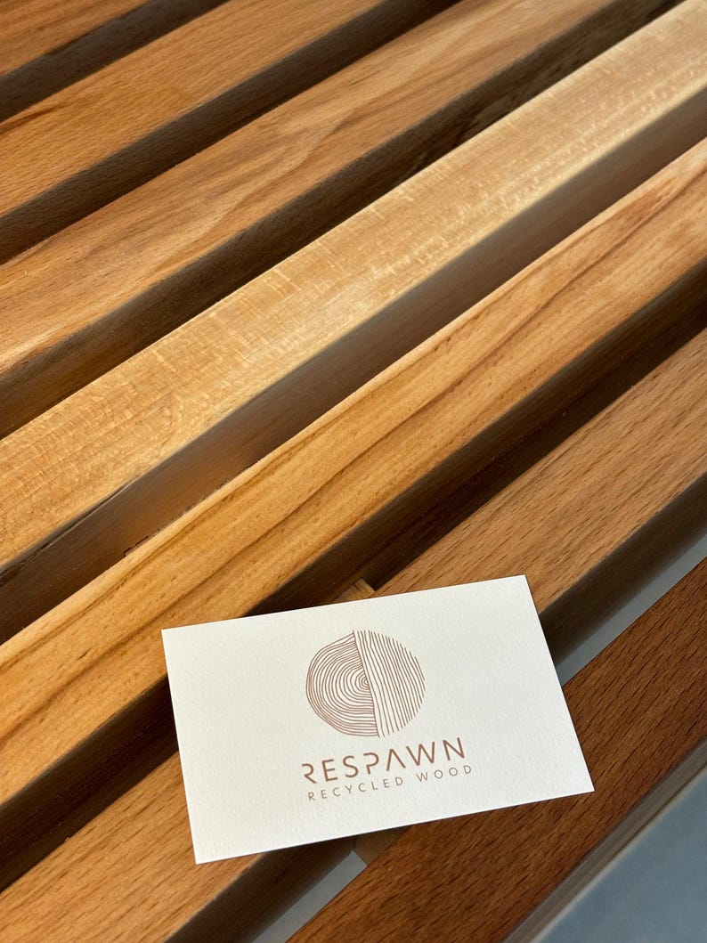 Une carte de visite blanche avec le logo de la marque Respawn Recycled Wood posée sur les lattes en bois du banc.