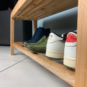 Vue rapprochée de profil de l'étagère inférieure en bois du banc, montrant plusieurs paires de chaussures de différentes couleurs alignées.