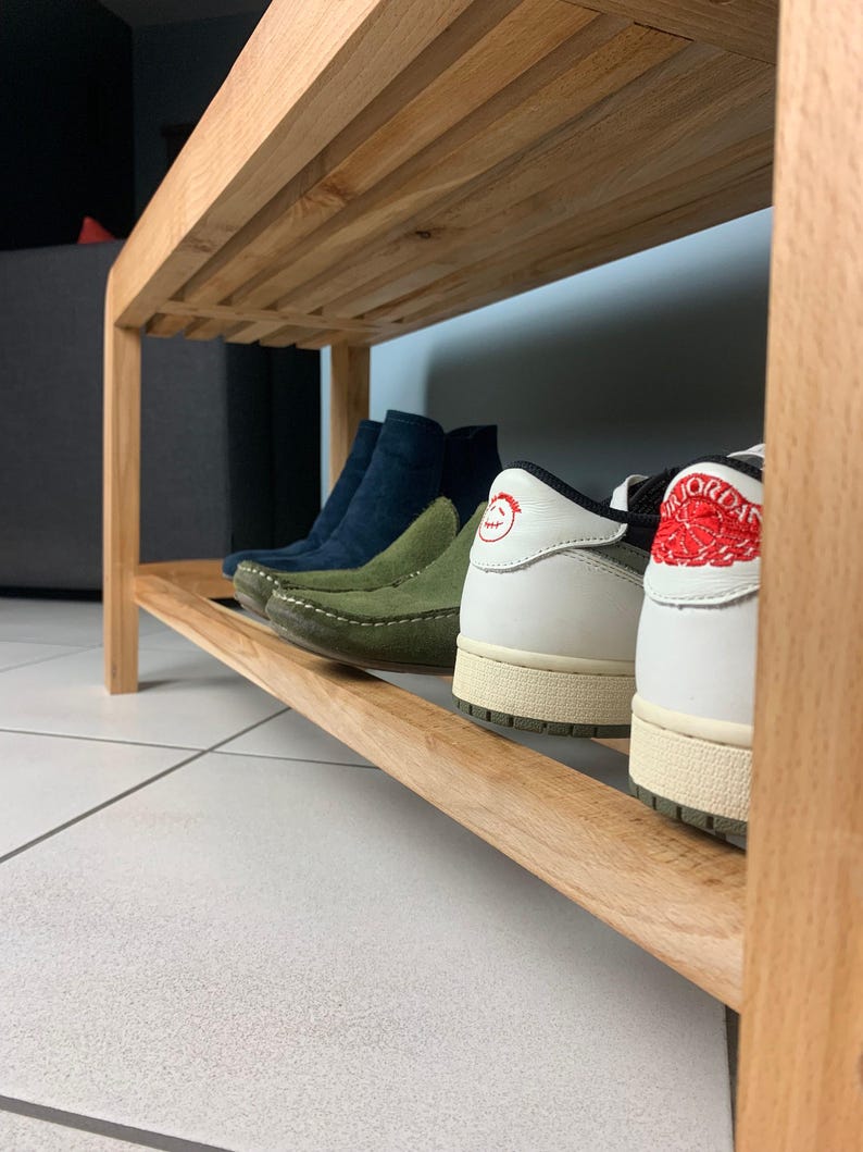 Vue rapprochée de profil de l'étagère inférieure en bois du banc, montrant plusieurs paires de chaussures de différentes couleurs alignées.