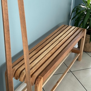 Vue en angle du banc en bois à lattes, avec deux montants verticaux en bois positionnés au premier plan à gauche.