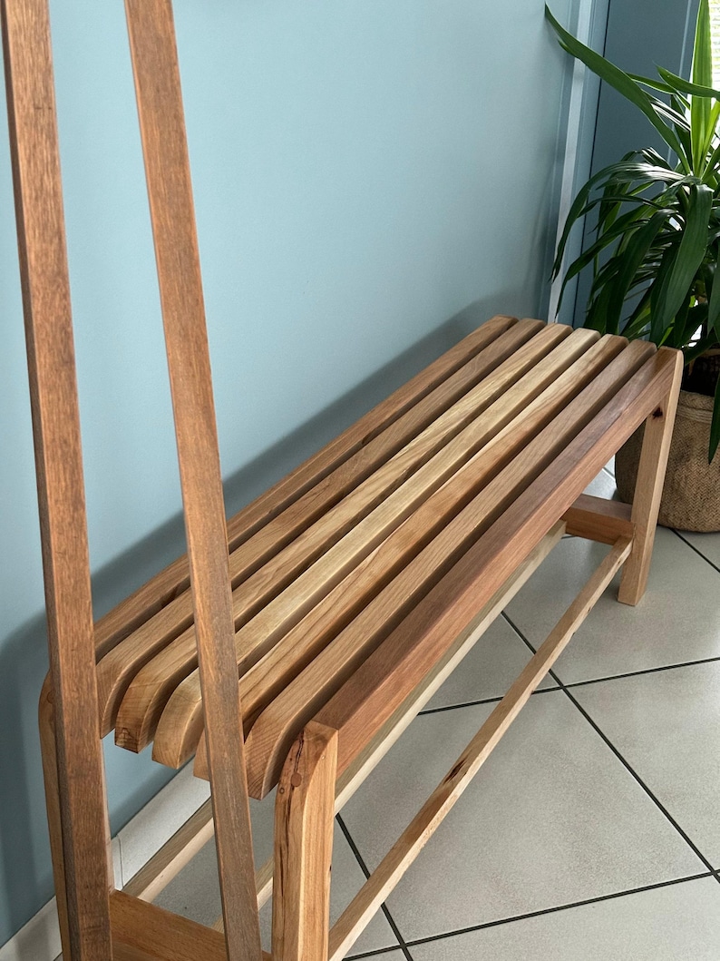Vue en angle du banc en bois à lattes, avec deux montants verticaux en bois positionnés au premier plan à gauche.