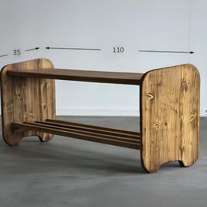 May include: A wooden shoe rack with a rustic finish. The rack has two shelves and measures 43 inches long, 14 inches wide, and 20 inches high. The wood grain is visible, and the design is simple and functional.