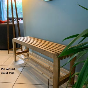 Un banc à chaussures en pin massif installé dans une pièce lumineuse près d'une plante verte, avec le texte Pin Massif Solid Pine incrusté.