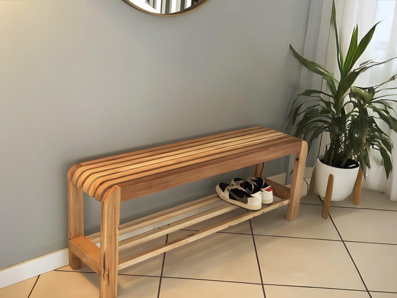 Un banc à chaussures en bois à lattes disposé le long d'un mur gris dans une entrée, avec une paire de chaussures de sport sur l'étagère inférieure.
