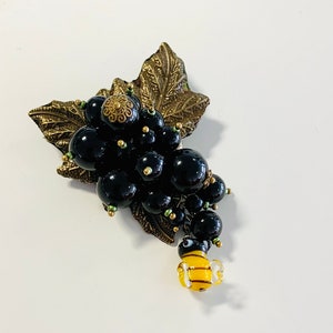 Peut inclure: Une broche en forme de grappe de perles noires en verre avec un motif de feuilles dorées et un charme d'abeille en verre jaune.