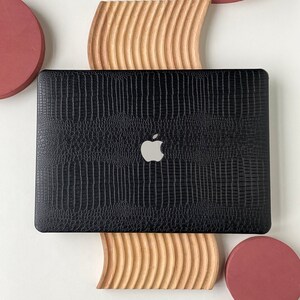 May include: A black laptop computer with a textured cover and an Apple logo on the lid. The laptop is sitting on a wooden stand with a curved design. There are three red circles around the laptop.