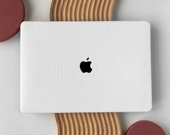 Op de afbeelding: Witte laptop met een krokodillederen patroon op de deksel en een Apple-logo. De laptop staat op een houten standaard met een golvend ontwerp. Er zijn twee rode cirkels aan weerszijden van de laptop.