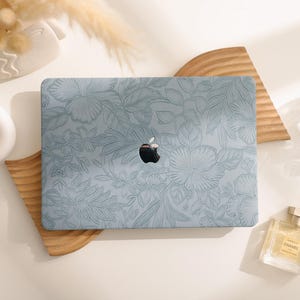 Könnte beinhalten: Ein hellblauer Laptop mit einem floralen Design auf der Abdeckung. Der Laptop steht auf einer Holzoberfläche.