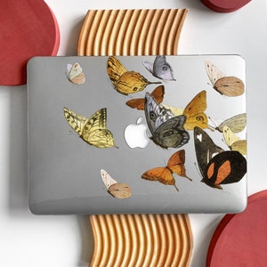 May include: A silver laptop with a variety of colorful butterfly stickers on the lid. The laptop is sitting on a wooden stand with two red circles on either side.