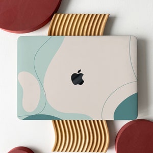 Pode incluir: Um computador portátil com um design abstrato branco e azul claro na tampa. O laptop está em um suporte de madeira com um padrão ondulado. Há dois círculos vermelhos de cada lado do suporte.