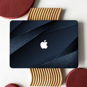 Peut inclure: Un ordinateur portable bleu foncé avec un design géométrique et un logo Apple blanc. L'ordinateur portable est posé sur une surface en bois avec un cercle rouge de chaque côté.