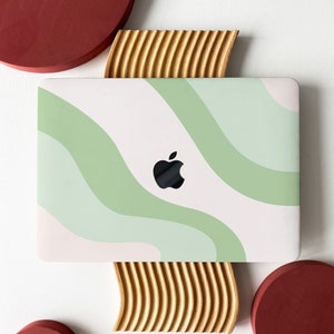 May include: A white laptop with a green and white abstract wave design on the lid. The laptop is sitting on a wooden stand with a red circle on either side.