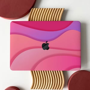 May include: A pink and purple laptop skin with a wavy design. The skin has a black Apple logo in the centre.
