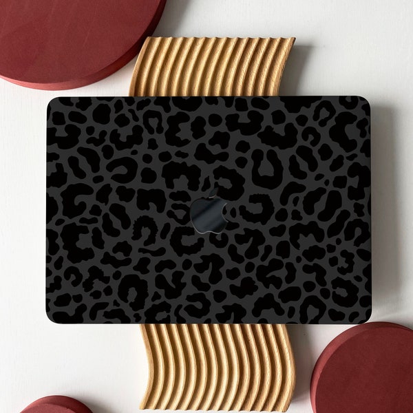 May include: A black laptop computer with a leopard print design on the cover. The laptop is sitting on a wooden surface with two red circles on either side.