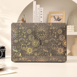 Op de afbeelding: Een laptop skin met een hemels ontwerp met gouden zonnen, manen en sterren op een zwarte achtergrond.