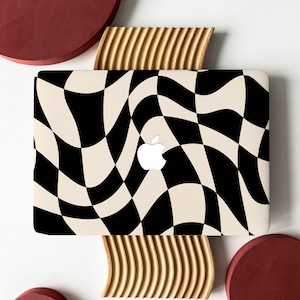 May include: A laptop computer with a black and white chequered pattern on the lid. The laptop is sitting on a wooden surface with a red circle on either side.