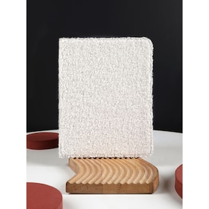 May include: A white fluffy notebook cover with a textured surface. The cover is sitting on a wooden stand with a wavy design.