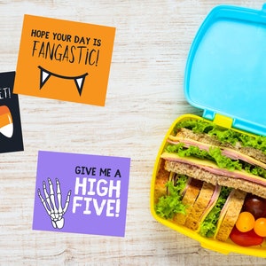May include: Three Halloween-themed lunchbox notes with fun sayings. The notes say "You are too sweet!" with candy corn, "Hope your day is Fangastic!" with fangs, and "Give me a High Five!" with a skeleton hand.
