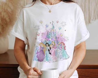 May include: White t-shirt with a colorful illustration of Disney princesses in front of Cinderella's castle with fireworks and balloons.