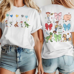 May include: White t-shirts with colorful cartoon character graphics. One shirt features characters holding balloons, the other has various characters and bows. The designs include a cowboy, a space ranger, a dinosaur, and a pig.