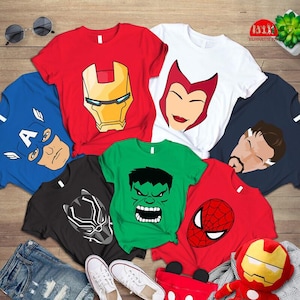 Może przedstawiać: Kolekcja koszulek z krótkim rękawem z nadrukami graficznymi superbohaterów, w tym Iron Mana, Kapitana Ameryki, Scarlet Witch, Doktora Strange'a, Czarnej Pantery, Hulka i Spider-Mana, ułożonych na drewnianej powierzchni.