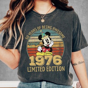 A person wearing a t-shirt with a vintage Mickey Mouse design and text that reads "50 YEARS OF BEING AWESOME" and "LIMITED EDITION 1976".