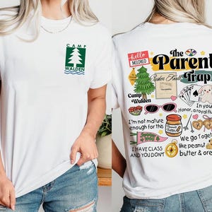 May include: White t-shirt with a green and white Camp Walden logo on the front. The back features a colorful graphic with the text "The Parent Trap," along with various illustrations and phrases, including "In your honor, a royal flush."