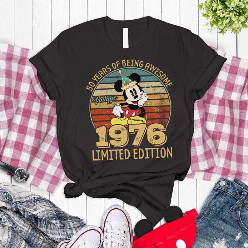 A black t-shirt with a vintage-style graphic of Mickey Mouse and the text "50 YEARS OF BEING AWESOME" printed on it, along with the year "1976" and the text "LIMITED EDITION".