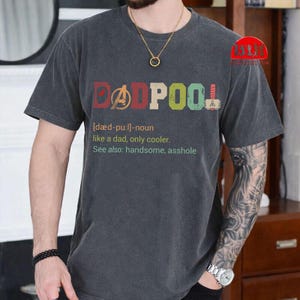 May include: Dark gray t-shirt with the word "DADPOOL" in colorful letters. The shirt includes the definition: "like a dad, only cooler. See also: handsome, asshole."