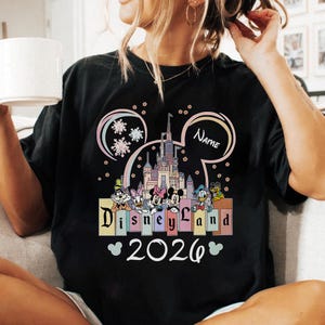 A person wearing a black t-shirt with a Disney Land-themed graphic and the text "Disneyland 2020" printed on it.