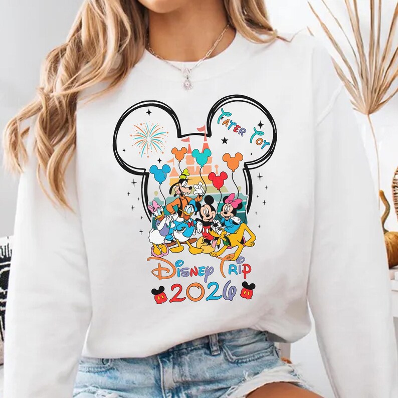 A white sweatshirt with a colorful graphic design featuring Disney characters and the text "Disney Trip 2020".