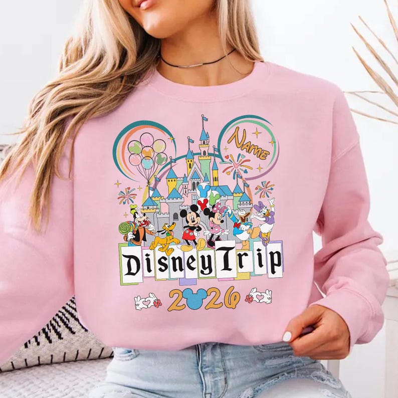 A woman wearing a pink sweatshirt with a Disney-themed graphic and text.