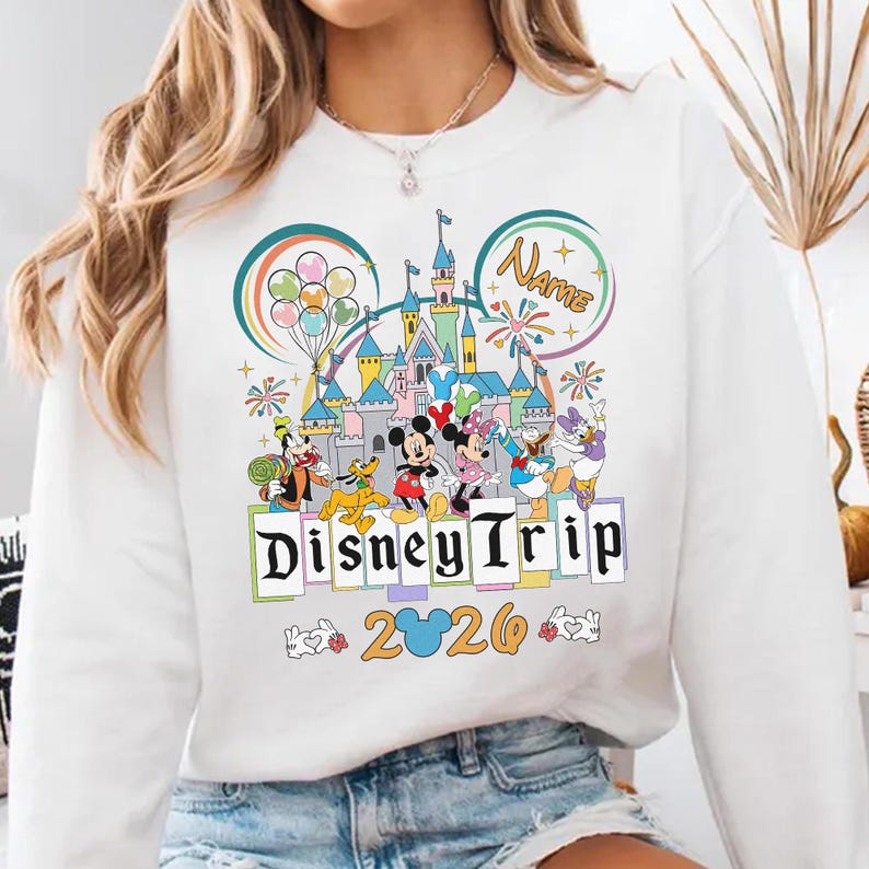 A person wearing a white sweater with a Disney-themed graphic printed on it.